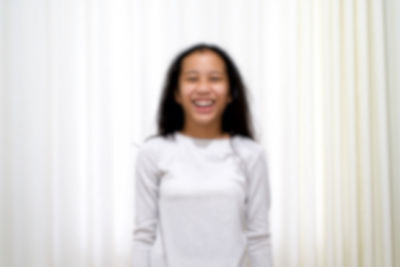 Portrait of a smiling young woman standing against white wall
