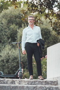 Full length of businessman with electric scooter standing outdoors
