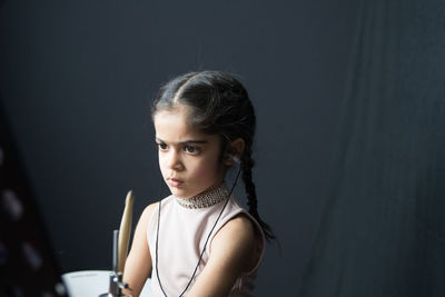 Girl wearing hearing aid while playing drum against wall