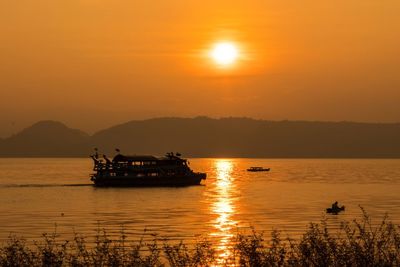 Silhouette boat in sea against orange sky