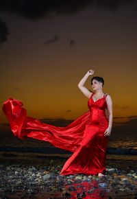 Young woman with red umbrella standing on beach during sunset