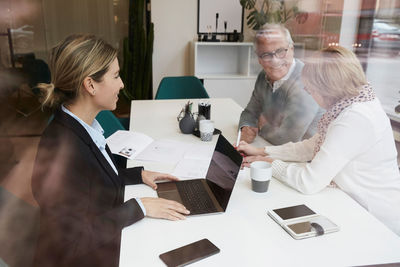 Female estate agent discussing with senior couple over property documents in office