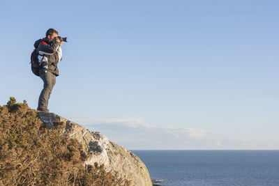 Man photographing on rock by sea against sky