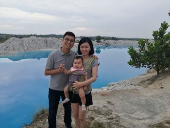 Portrait of happy family standing by river against sky