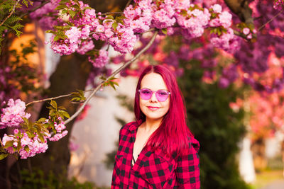 Portrait of smiling young woman standing by pink flowering tree