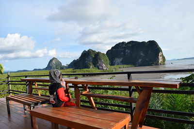 Man on bench by railing against sky