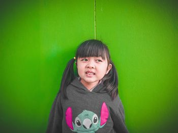 Smiling girl looking away while standing against green wall