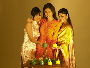 Smiling young friends with oil lamps against wall