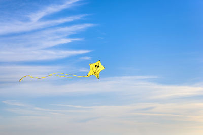 Low angle view of yellow kite flying against blue sky