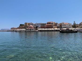 Buildings by sea against clear blue sky