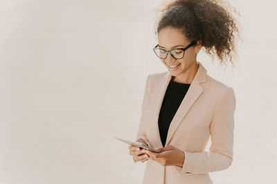 Young woman using phone while standing against white background