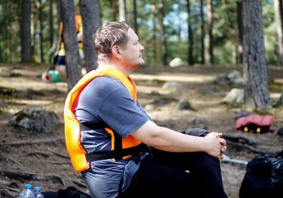 Side view of mature man wearing life jacket looking away while sitting in forest