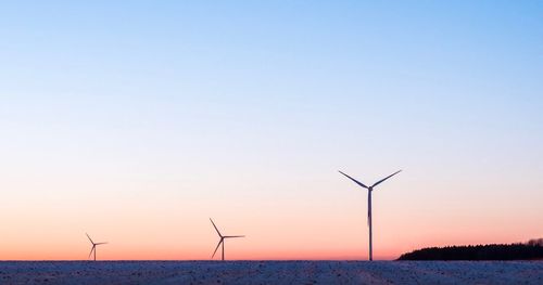 Wind turbines on landscape against sky during sunset