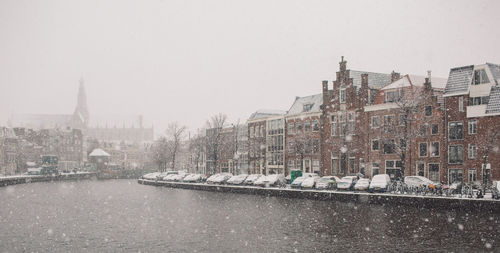River by buildings against sky during snowfall