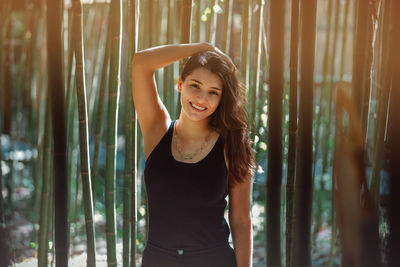 Young latina woman smiling at the camera, in front of bamboo and sunlight coming form the background