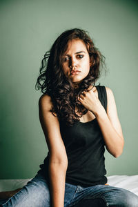 Portrait of beautiful young woman sitting against wall