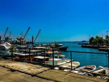 Boats moored at harbor against clear blue sky