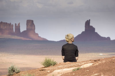 Rear view of woman sitting on rock against sky