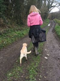 Rear view of girl walking with dog on dirt road