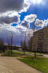 Footpath by bare trees and buildings against sky