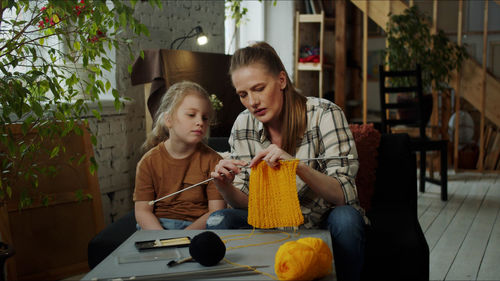 Mother teaching crocheting to daughter at home