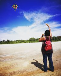 Rear view of woman flying kite at beach against sky on sunny day