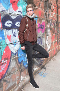 Full length of young man standing by graffiti wall