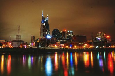 River by illuminated cityscape against sky at night