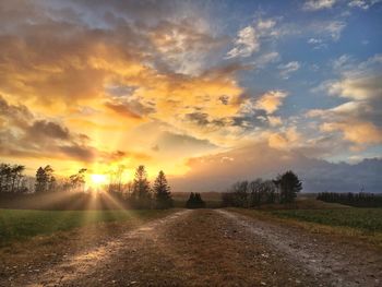 Road amidst field against sky during sunset