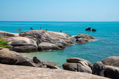 Rocks by sea against clear blue sky