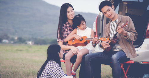 Friends spending leisure time against car on field 