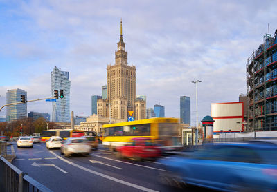 Cars on road by buildings against sky in city