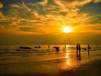 Silhouette people on beach against sky during sunset