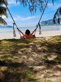 Rear view of man sitting on shore at beach against sky
