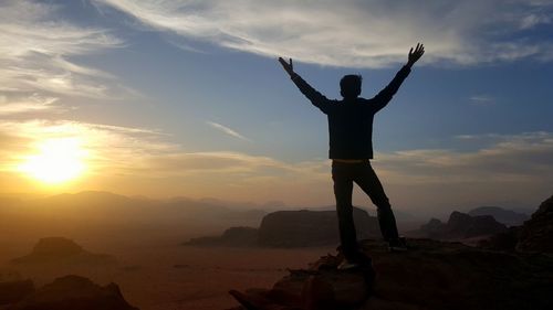 Boy standing on rock formation against sky during sunset