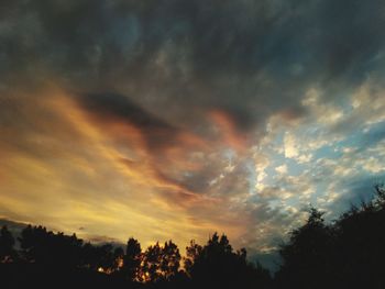 Low angle view of silhouette trees against dramatic sky