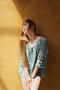 Beautiful young woman standing against wall