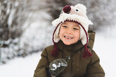 Cute little boy in funny winter hat walks during a snowfall. outdoors winter activities for kids.