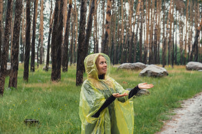 Portrait of young woman with arms raised standing in forest