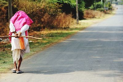 Rear view full length of man holding stick on road