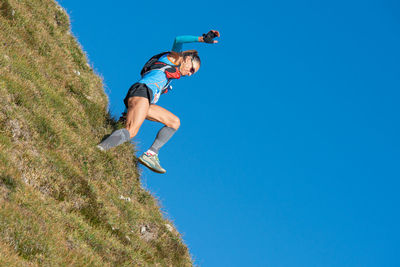 Low angle view of man jumping on mountain against clear blue sky