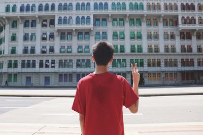 Rear view of man standing on street against building in city