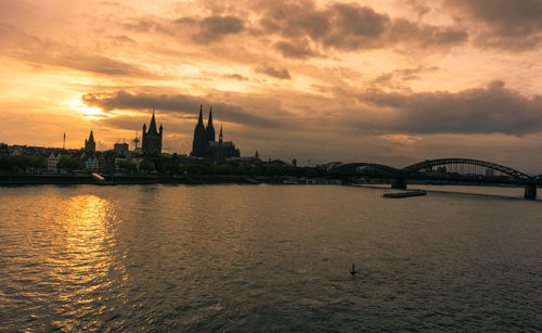 Scenic view of river by buildings against sky during sunset