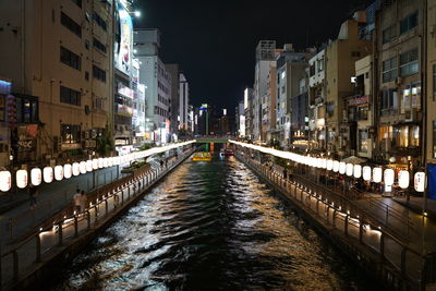 Illuminated bridge over river amidst buildings in city at night