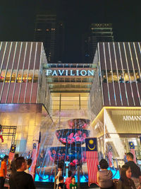 Low angle view of crowd at illuminated city against sky at night