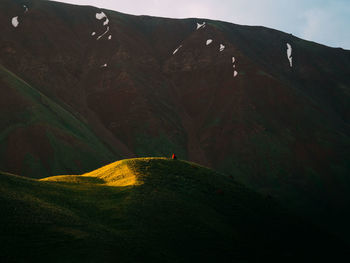 Mid distance view of man sitting on mountain against sky