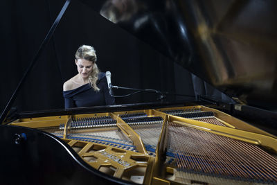 Mature pianist playing grand piano against black background