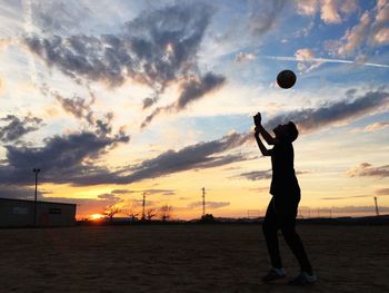 Silhouette young man playing soccer on playground against cloudy sky during sunset