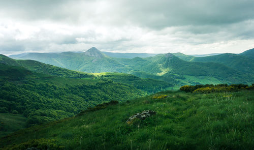 Scenic view of green mountains against cloudy sky