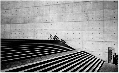 Man by bicycle sitting on steps against wall